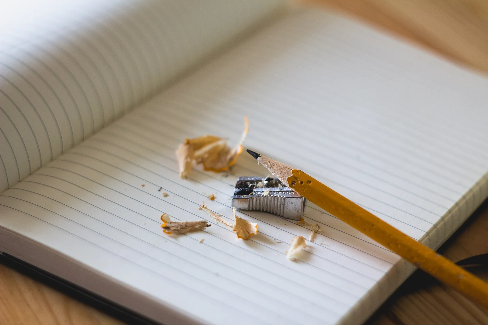 A sharpened yellow pencil and pencil shavings resting on an open ruled notebook.