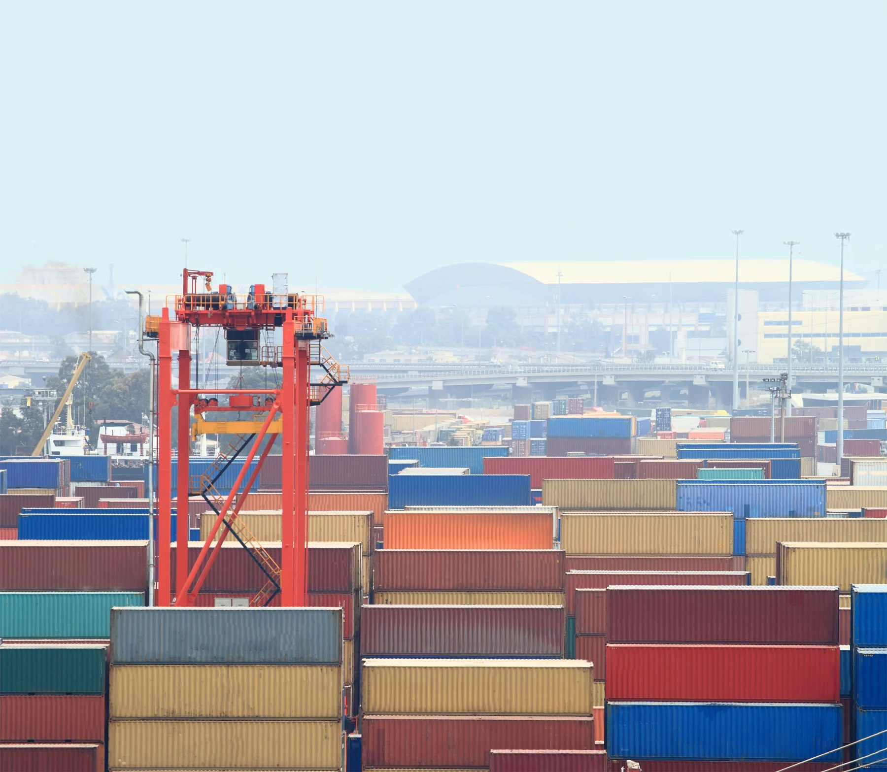 A red container-handling crane among stacks of colourful shipping containers at a port.
